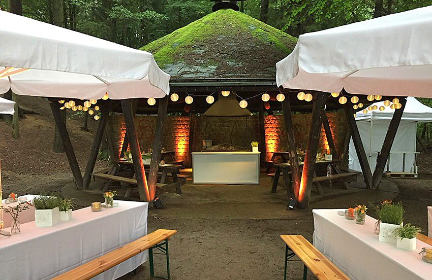 Eine Grillhütte in einem Wald, festlich dekoriert, davor Tische und Bänke